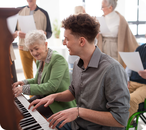 A young man plays piano while a group of adults sings along